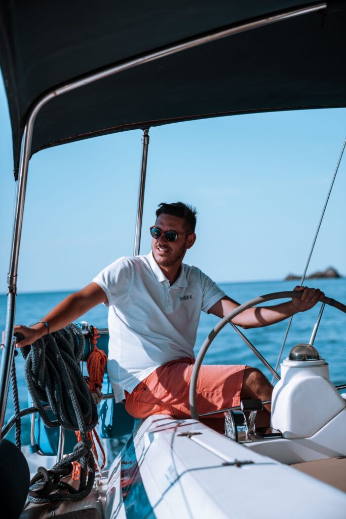 Un hombre al timón de un yate bajo un sol radiante, que transmite el estilo náutico y la aventura en mar abierto.